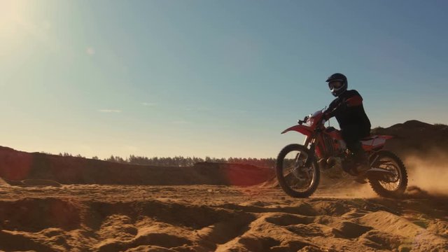 Side View Footage of the Professional Motocross Motorcycle Rider Driving on the Dune and Further Down the Off-Road Track. It's Sunset and Track is Covered with Smoke/ Mist. 4K UHD.