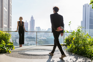 Stylish young man in a suit walking towards a beautiful lady while hiding a gift behind his back