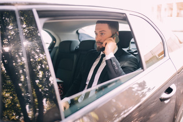 Young businessman talking on mobile phone and looking away while sitting on the back seat of a car