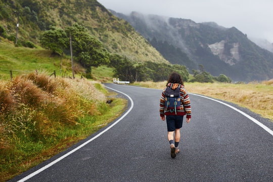 Back view of backpacker walking down the remote road
