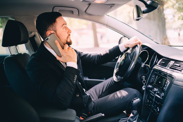 Handsome young businessman talking on his smart phone and smiling while sitting on the front seat