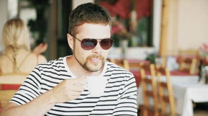 Young bearded man having coffee in a street cafe on his vacation