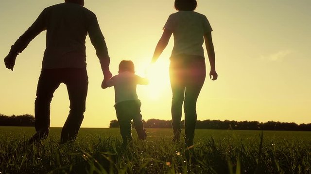 Happy young family with baby boy running around on summer field. A healthy mother, father and son enjoying nature together, outdoors. Sunset. Slow motion