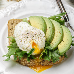 Toast with poached egg, avocado, lettuce, flax seed, spices. Breakfast. Selective focus, square picture