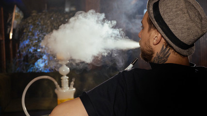 The guy is sitting on the sofa in the cafe and smoking a hookah © alexeg84