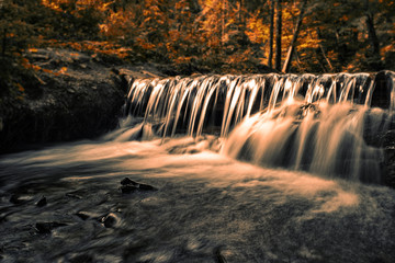 Waterfall in the autumn forest is illuminated by the sunbeams