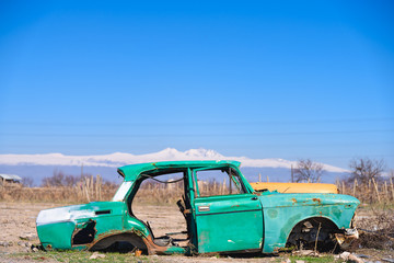 Abandoned and rusty wreck of an old green vintage Soviet Russian car and scenic snow-topped...