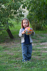 A little boy in jeans clothes plays with a bright ball in football. A funny kid in a hood holds a bright round ball.