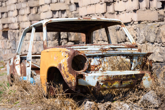 Abandoned and rusty skeleton of a Soviet Russian car growing hay inside by the side of the building exterior in Ararat province on 4 April 2017.
