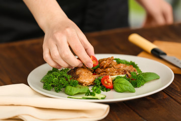 Woman decorating chicken dish with vegetables in kitchen