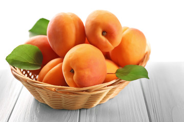 Wicker basket with fresh apricots on wooden table
