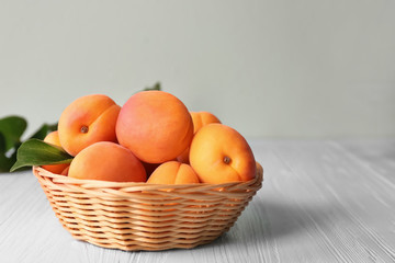 Wicker basket with fresh apricots on wooden table