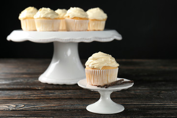 Tasty vanilla cupcakes on wooden table against black background