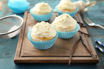 Tasty vanilla cupcakes on wooden board