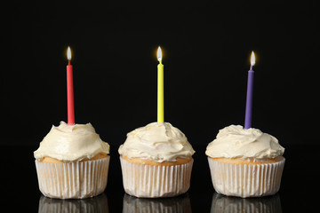 Tasty vanilla cupcakes with candles on black background