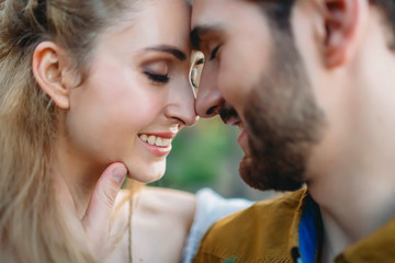A young couple smile and touching foreheads with closes eyes. Autumn wedding ceremony outdoors. Bride and groom look at each other with tenderness and love. Close-up portrait