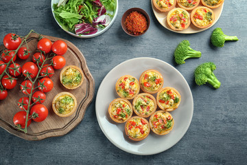 Composition with broccoli quiche tartlets and vegetables on table