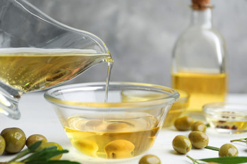 Pouring natural olive oil into glass bowl on wooden table