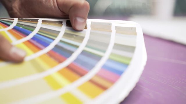 Side view of hands of an unrecognizable architect holding a color chart and looking at it. Handheld real time close up shot
