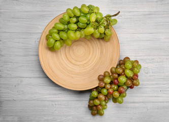 Fresh grapes and wooden plate on light background