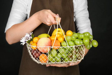 Woman holding metal basket with fresh fruits on black background