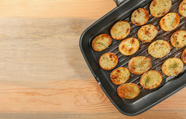 Grill pan with delicious baked potato slices on wooden background