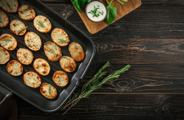 Grill pan with delicious baked potato slices on wooden background