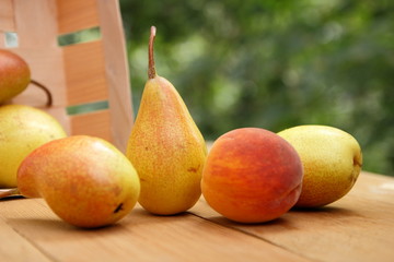 Pears and peaches in a wooden box on a wooden table at harvest in the forest