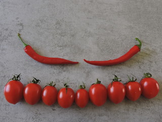 Cherry tomatoes in a line and chili peppers on a light gray background. Copy space. Top view.