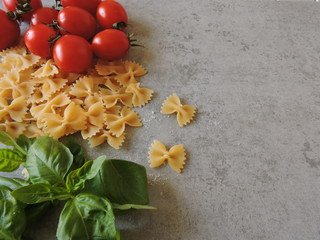 Pasta bows, cherry tomatoes, basil, olives, salt. Top view.