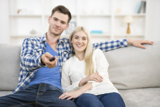The happy man and woman sit on the sofa and hold the remote control