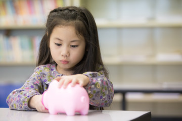 Asian Little girl holding a piggybank. Girl try to Save Money in Piggy Bank. Children with investment concept.