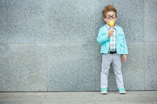 Fashion kid with lollipop near gray wall