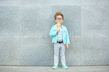 Fashion kid with lollipop near gray wall