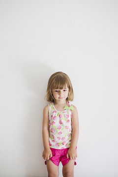 Portrait of shy little girl leaning against the wall