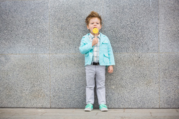 Fashion kid with lollipop near gray wall