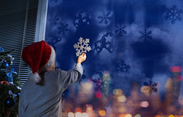 Little boy putting snowflake on the window 