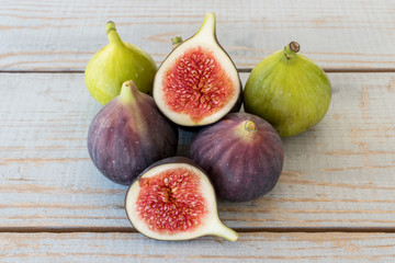 Whole figs and one fig sliced in half on top of a  garden table. Focus is on the sliced fig.