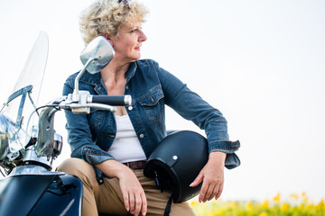 Portrait of an active senior woman wearing a blue denim jacket while sitting on a motorcycle in the...