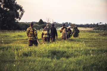 Scène de chasse avec un groupe d& 39 hommes chasseurs traversant de hautes herbes sur un terrain rural au coucher du soleil pendant la saison de chasse