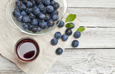 a glass of fresh juice from a plum, ripe plums in a bowl on a light background