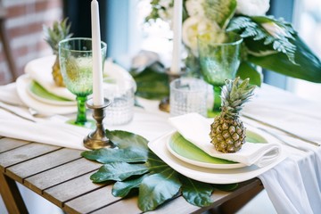plates on the table decorated with pineapples, candles and flowers, green and white colour