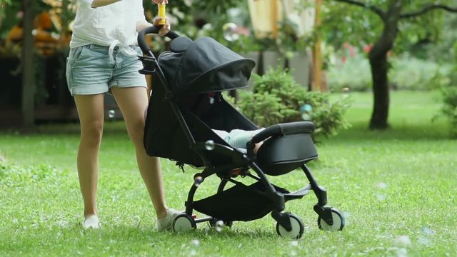 Mother blows bubbles during rocks her baby in a baby carriage