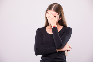 Girl with distrust and doubt looks forward, her arms near face on white