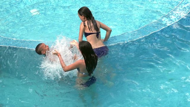 Young kids play splashing water in swimming pool