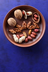 Walnuts and peanuts on a brown clay plate on a blue background