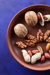 Walnuts and peanuts on a brown clay plate on a blue background