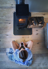 Young brunette woman sitting down on the floor by the fireplace in a wooden cabin. Top view from...