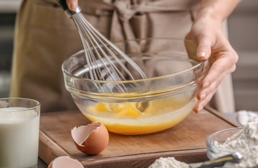 Female chef whisking eggs in glass bowl on kitchen table