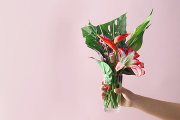 Woman holding vase with beautiful tropical flowers on color background